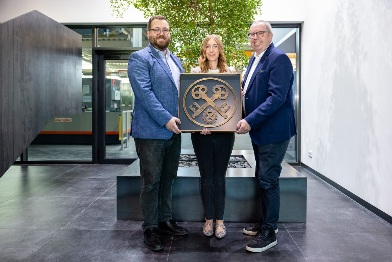 Drei Personen halten ein großes, symbolisches Schlüssel-Emblem in einem modernen Innenraum.