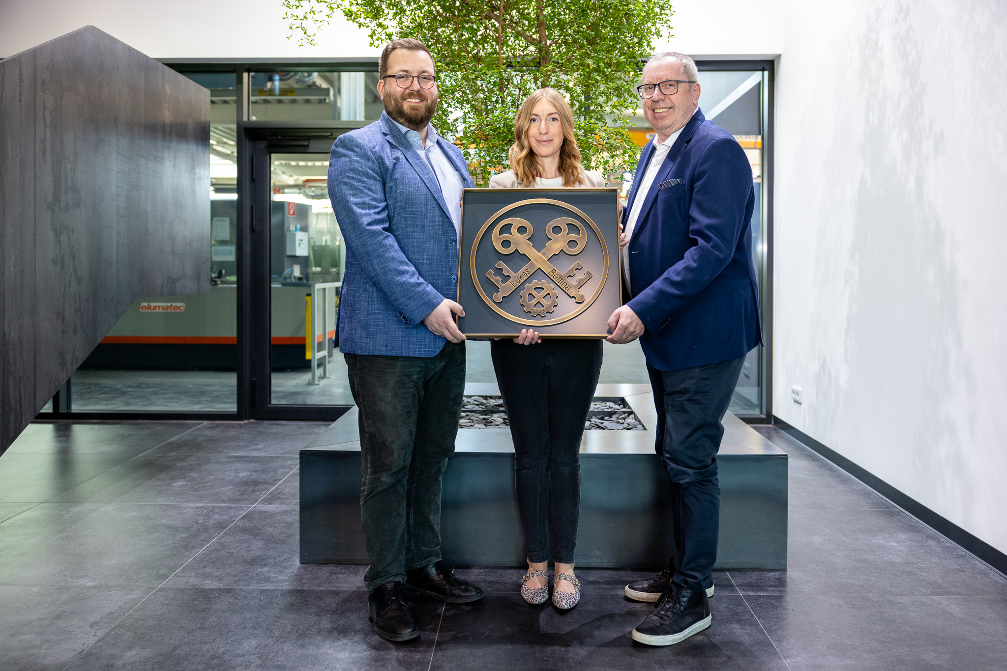 Drei Personen halten ein großes, symbolisches Schlüssel-Emblem in einem modernen Innenraum.